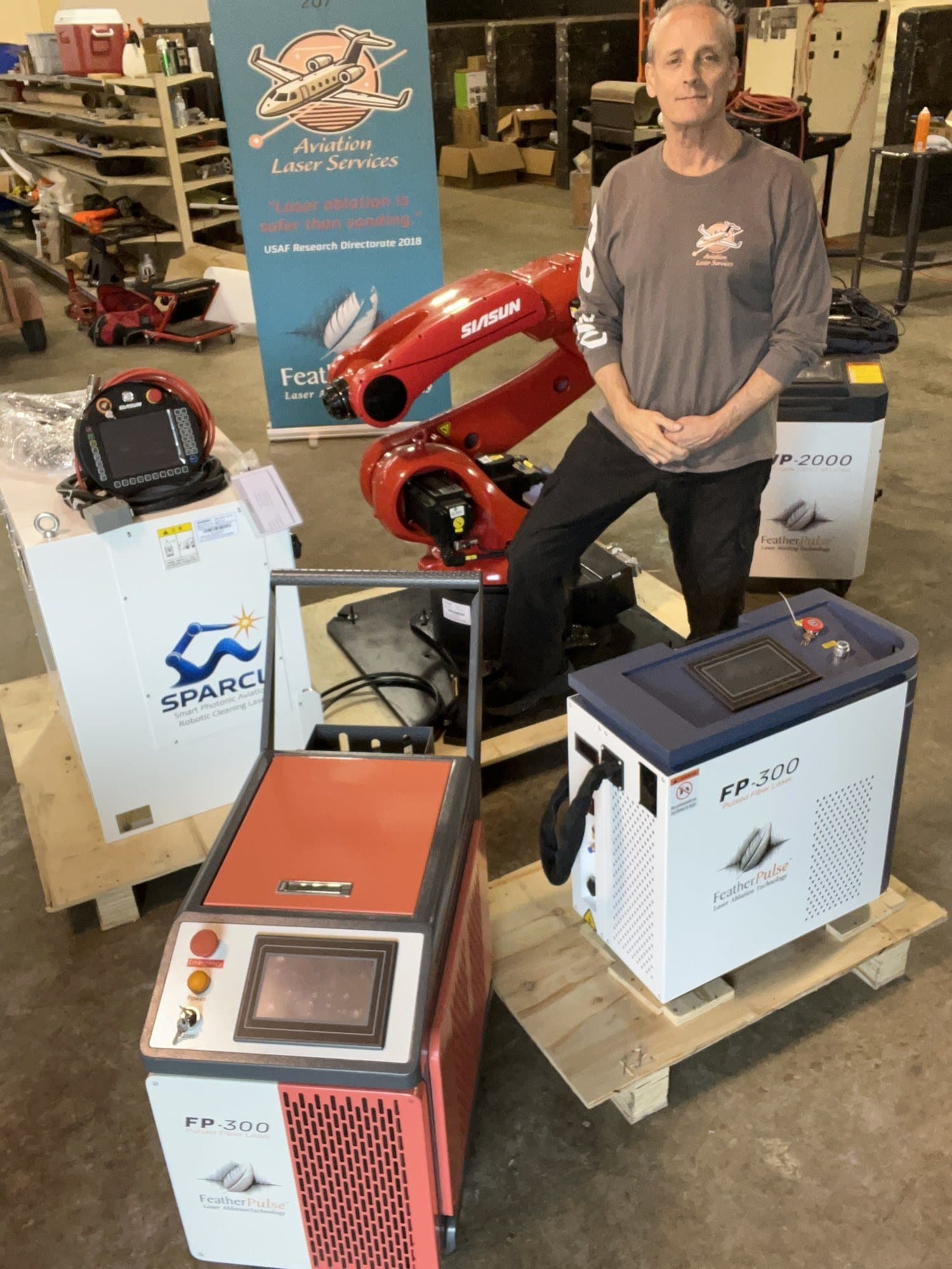 Gama completa de equipos de limpieza láser FeatherPulse junto a un brazo robótico industrial